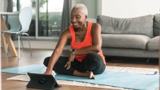 Person sitting on the floor in a room wearing exercise clothes and looking at a tablet