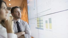 Two people standing in front of a large white board that has graphs on it