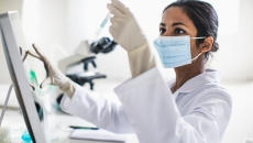 Scientist examining a test tube in a lab in front of a computer.