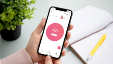 A person holding a smartphone displaying the app. The screen reads, "Period: Day 1."