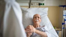 person in hospital bed holds hand of person in white lab coat