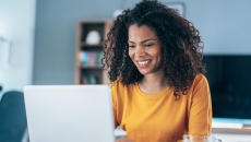 Person sitting in a house looking at a computer and smiling