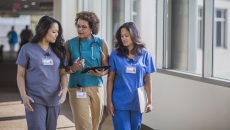 Three people walking down a hall, two healthcare providers in scrubs and one person in civilian clothing