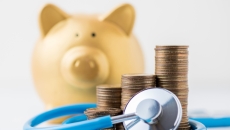 A piggy bank next to coins and a stethoscope