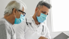 A medical professional and a patient talking to another provider using a tablet.
