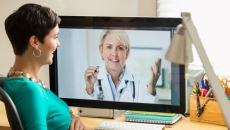 Person with green shirt talks with person on computer monitor in lab coat