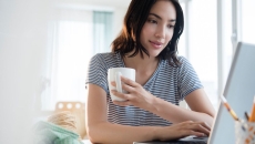 Person sitting at a computer while holding a cup of coffee