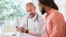 Healthcare provider and patient with an orange shirt sitting at a desk and looking at a tablet