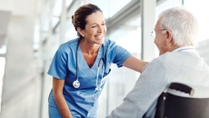 Person sitting in a wheelchair with a healthcare provider in scrubs standing over them