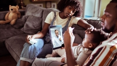 Three people sitting on a couch looking at a computer with a healthcare provider on the screen