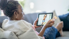 Person sitting on a couch holding a tablet on their lap with a healthcare professional on the screen