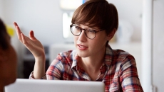 Person sitting at a computer with their hand up talking