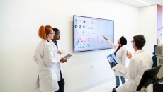 Four healthcare providers in a room looking at a screen with data on it