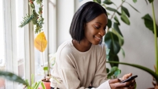 A person using a smartphone sitting by a window and surrounded by plants