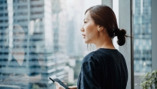 A young woman using a smartphone and looking out a window.