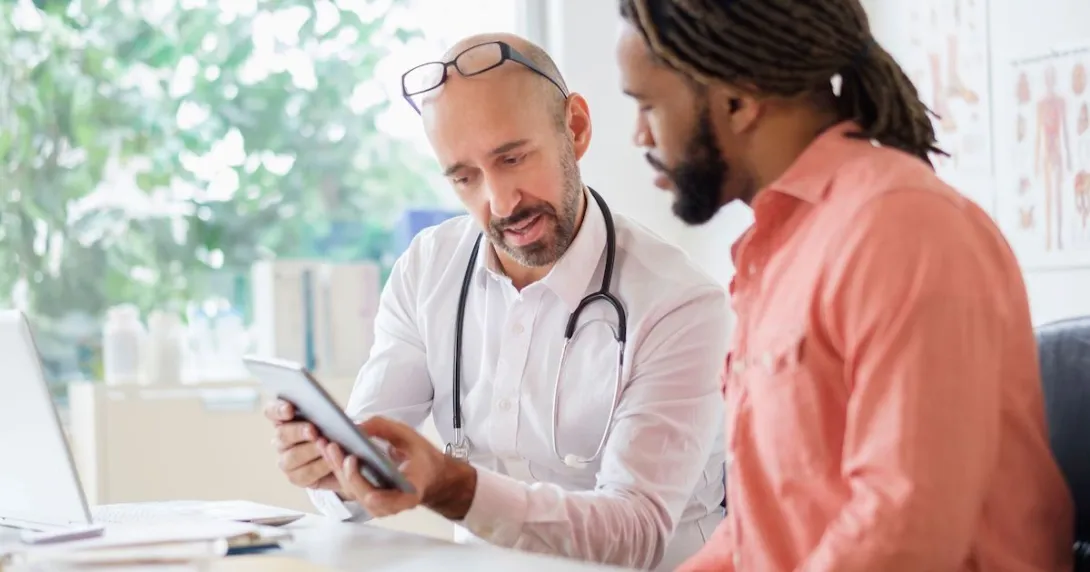 Healthcare provider sitting with a patient and showing them a tablet