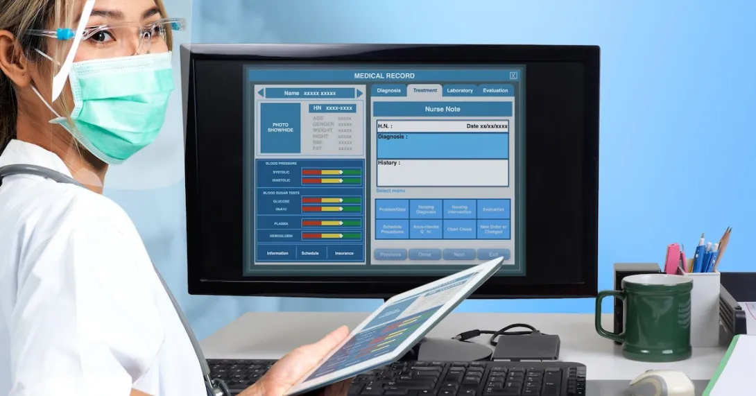 Healthcare professional standing in front of a computer with an EHR on the screen