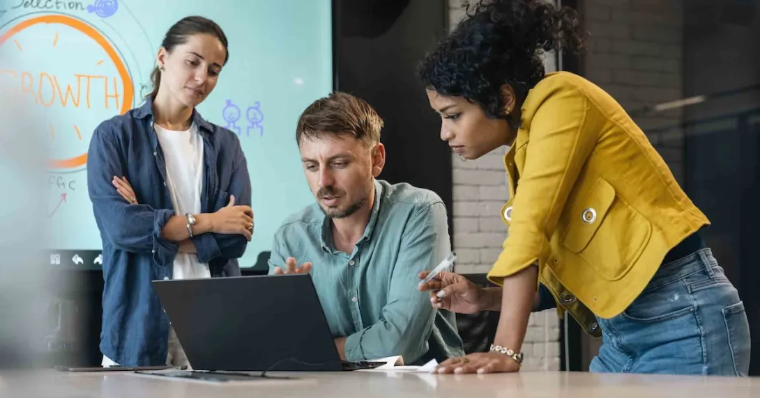 Three people in an office standing around a computer
