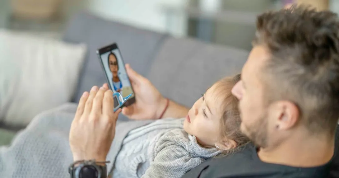 Person sitting on a couch with another person on their lap during a telemedicine call