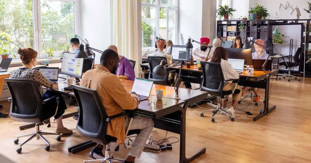 Numerous people sitting at large desks in a big room