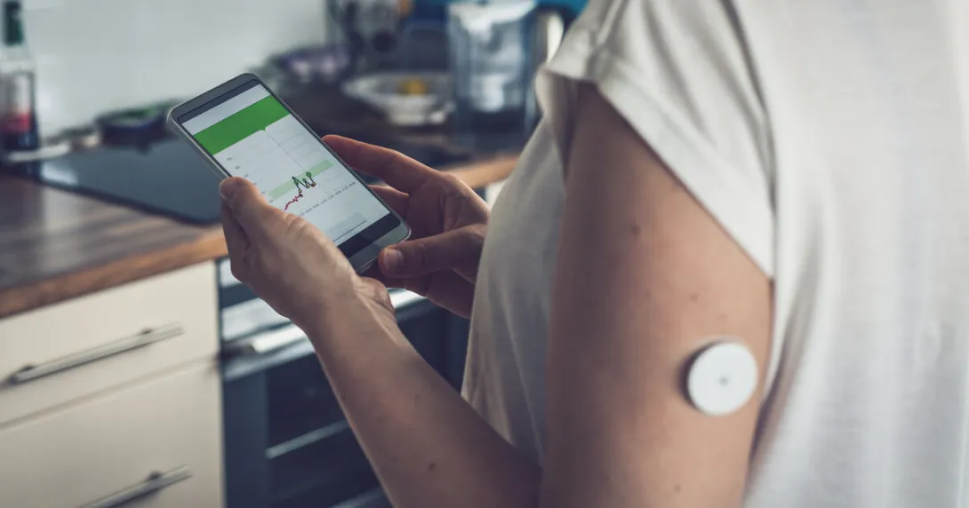 A patient wearing a remote sensor is checking their glucose level from a smartphone