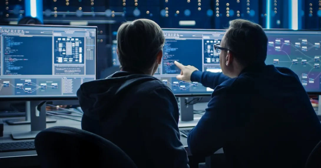 Two people sitting in front of two computer monitors looking at data on the screens