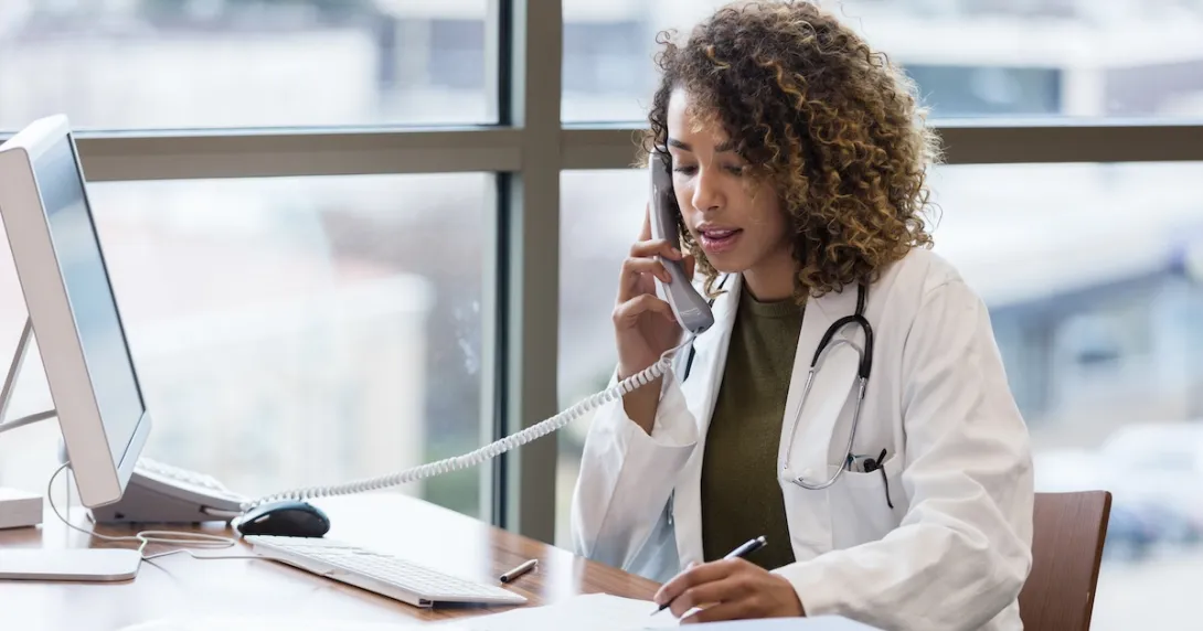Healthcare provider on the phone while sitting at a desk with a computer on it