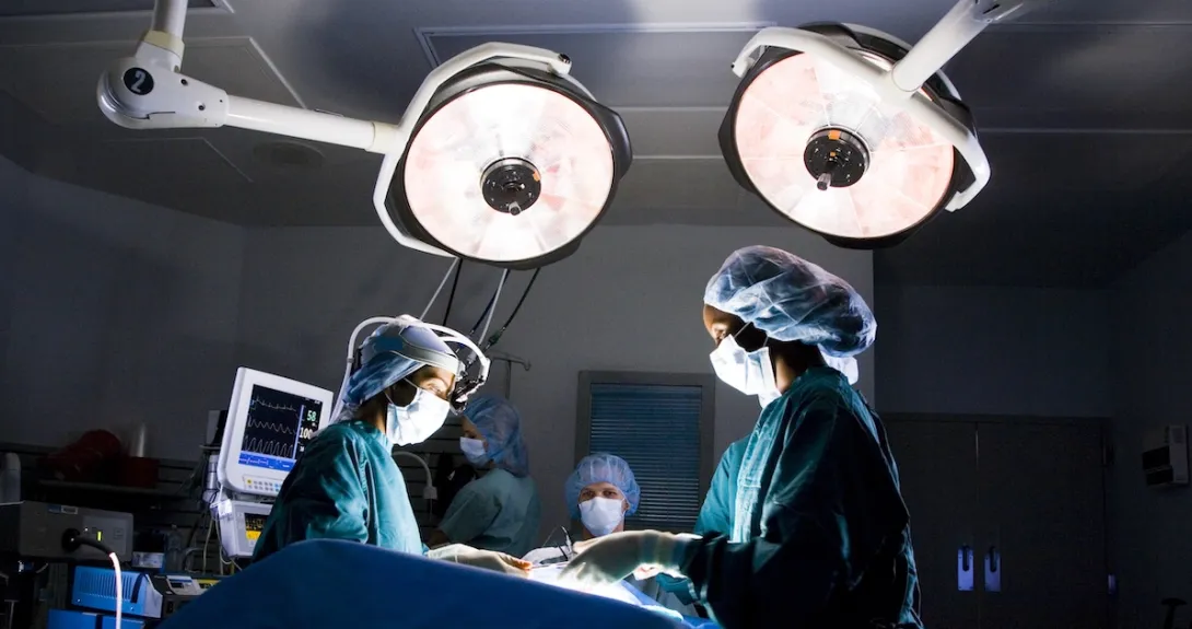 Surgeons in an operating room standing above a patient on a table with large lights above them