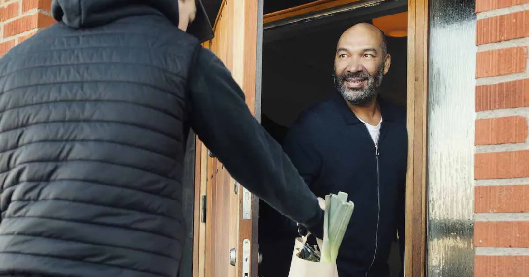 Person answering their front door and getting a delivery from another person