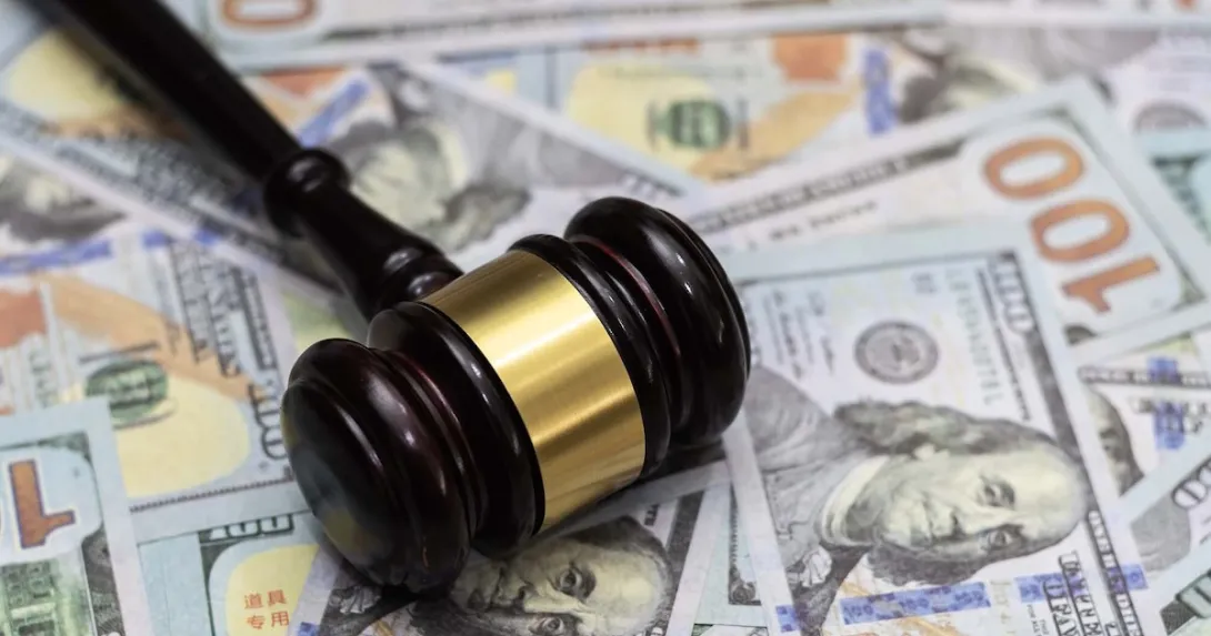 A gavel lying on a pile of hundred dollar bills.