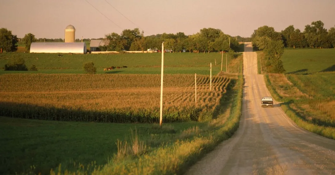 A truck driving on a gravel road near a farm