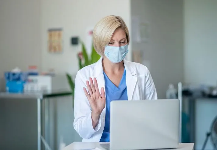 A doctor wearing a mask talking to a patient via telehealth