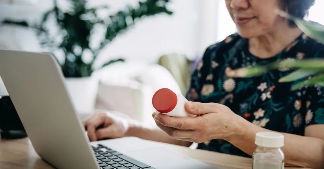 A woman holding a pill bottle and using a laptop.