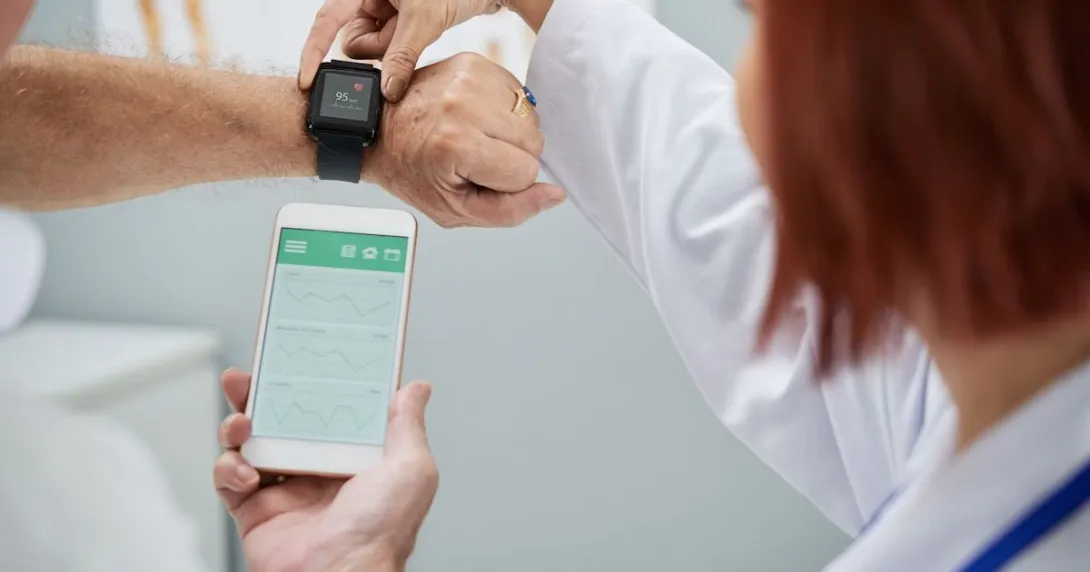 A doctor showing a senior patient how to synchronize their health app in a smartphone and a smartwatch