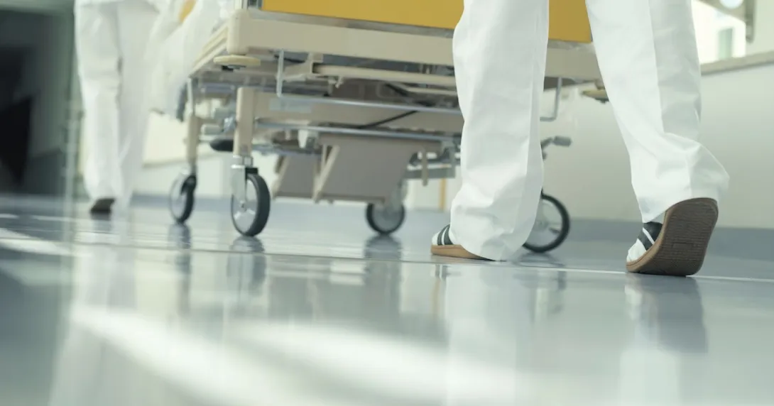 The legs of healthcare professionals pushing a hospital bed through a hallway