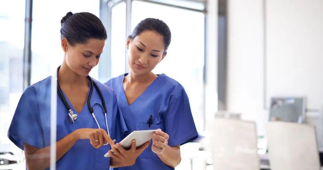 Two healthcare providers wearing blue scrubs and looking at a tablet