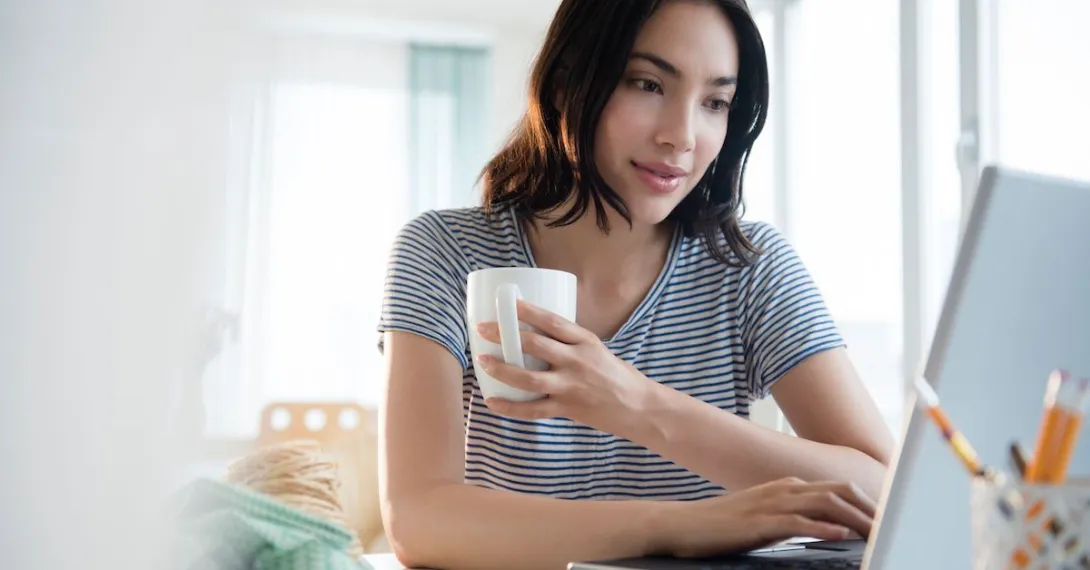 Person sitting at a computer while holding a coffee cup