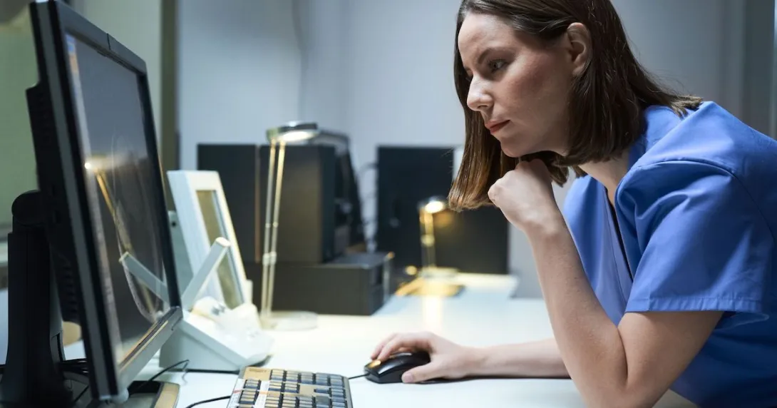 Healthcare provider sitting at a desk looking at a screen with their hand on the mouse