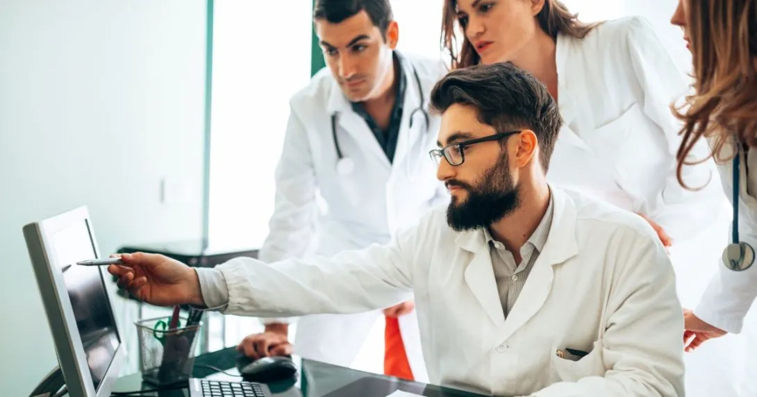 Three people wearing lab coats with one seated and pointing at screen