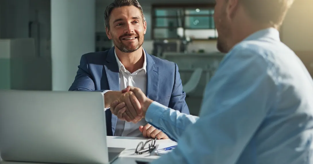 Two people sitting on opposite sides of a table while shaking hands