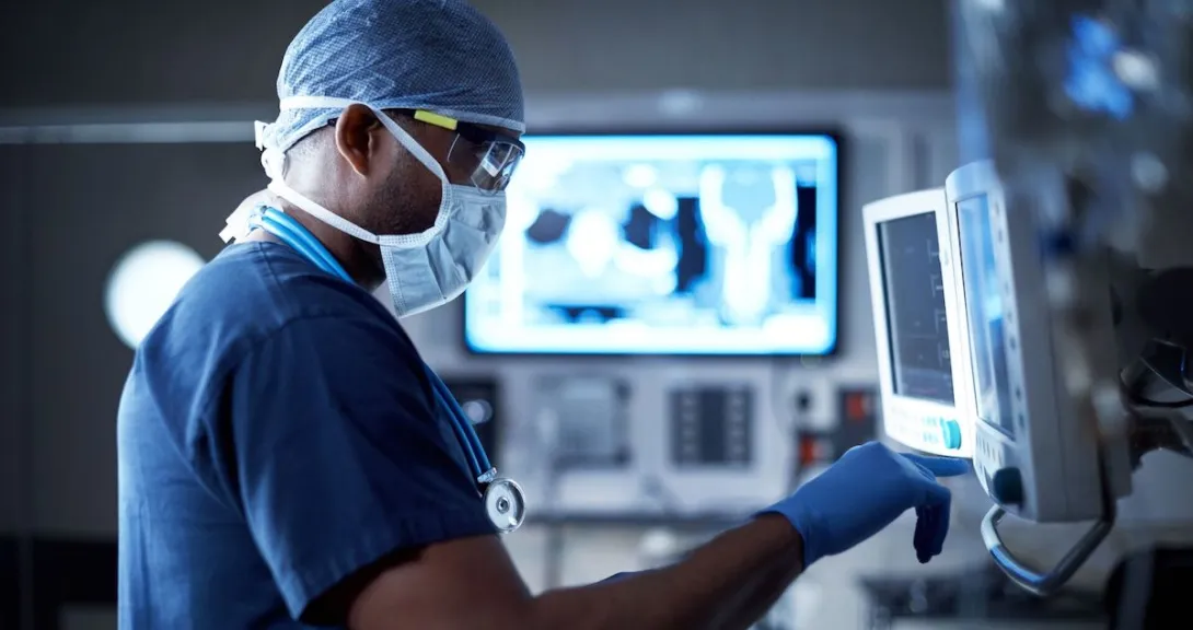 Healthcare provider wearing scrubs and a face mask while looking at screens with diagnostic images on them