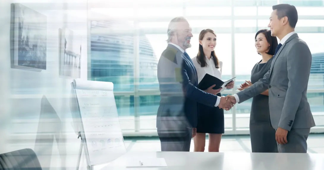 Two people standing in a room shaking hands while two other people stand by them and watch