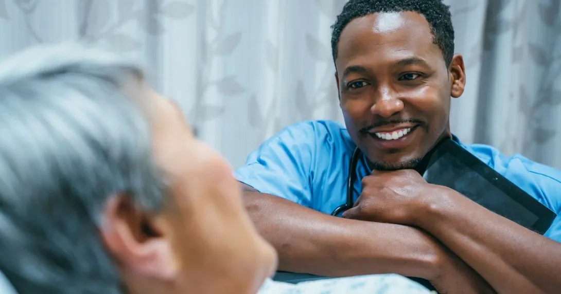 Nurse leaning against a patient's bed while the patient looks at them