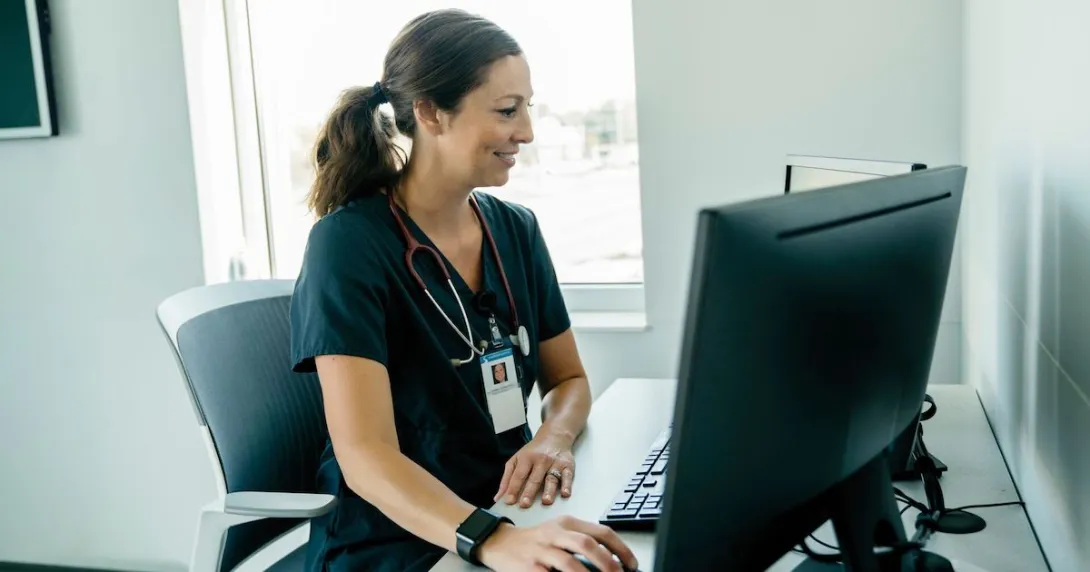 Person wearing nursing scrubs sitting at desktop