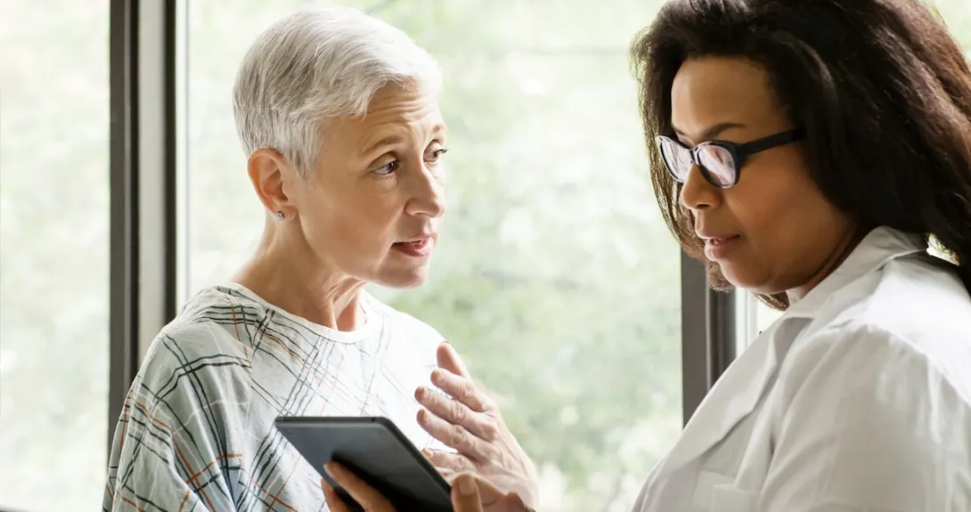 Healthcare provider standing next to a patient while looking at a tablet