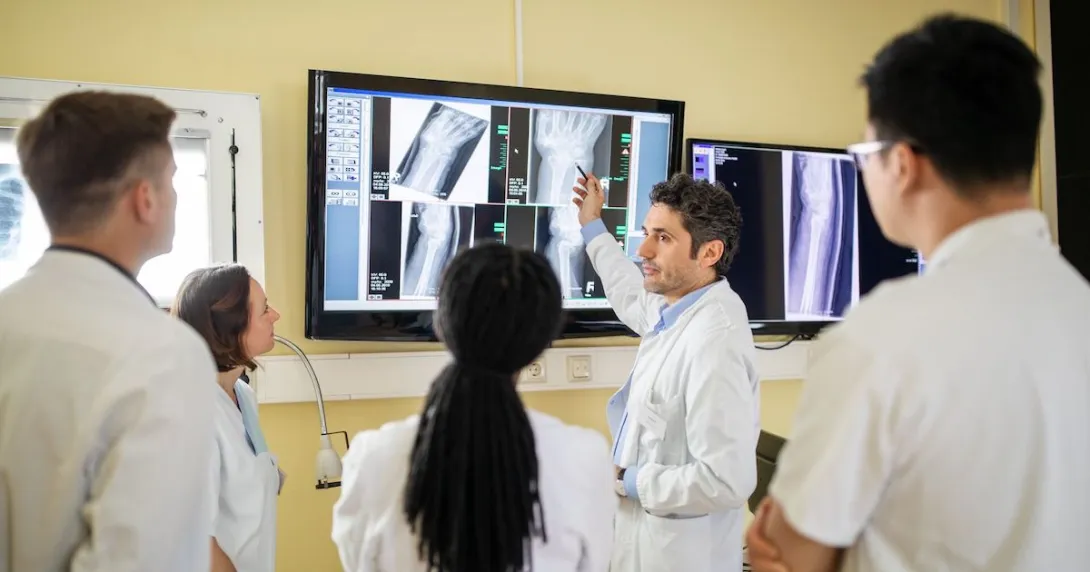 A group of clinicians discussing an X-ray report on a television screen